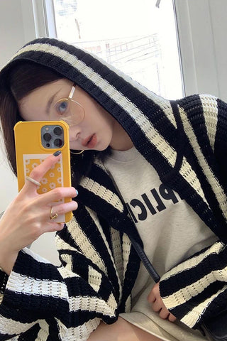 Person wearing a black and white striped hoodie with a phone in front of a window.