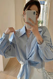 Person wearing a light blue shirt with a knot at the waist, taking a mirror selfie.