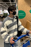 Person wearing a striped sweater and black mask, holding a blue shopping cart in a store.
