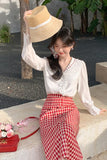Woman wearing a straw hat and white blouse with red checkered skirt outdoors.
