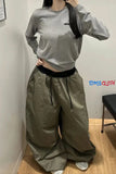 Person wearing a gray cropped sweatshirt and olive green wide-leg pants, standing against a plain wall.