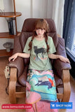 Woman sitting in a brown chair wearing a green t-shirt with a cat design and a colorful skirt.