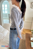 Woman wearing a gray sweater with ruffled collar and blue jeans in a living room.