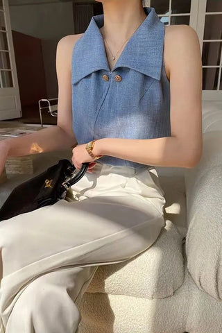 Person wearing a blue sleeveless top and white pants, sitting on a couch.