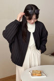 Woman wearing a black jacket and white dress, holding sunglasses indoors.