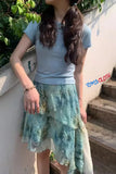 Person wearing a light blue top and green lace skirt outdoors.