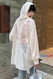 Person wearing a sheer white hoodie with feather patterns in an urban setting.