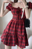 Red plaid dress with a white bow worn by a person, holding a black handbag.