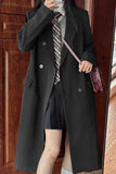 Person wearing a long black coat with a striped tie and holding a pink bag, standing in front of a wooden door.