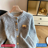 Gray cardigan with wooden buttons on a hanger against a neutral background