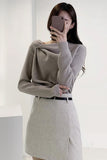 Person wearing a gray sweater and skirt, taking a mirror selfie.