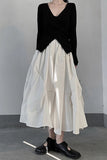 Person wearing a black top and white skirt against a gray background