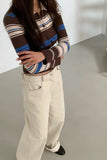 Person wearing a striped sweater and beige pants on a neutral background