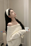 Woman wearing a white off-shoulder sweater holding a cup indoors.