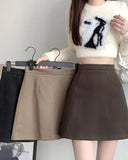 Person holding a hanger with a brown skirt, wearing a white sweater with black design.