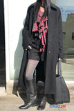 Person wearing a long dark coat, black boots, and a red plaid scarf with a blurred background.