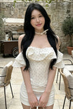 Woman in a white dress standing outdoors with a stone wall and chairs in the background