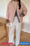 Person wearing a pink puffer jacket and white pants in a minimal indoor setting with 'tomscloth.com' branding.