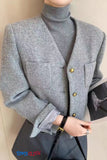 Person wearing a gray blazer with gold buttons against a neutral background