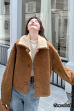 Person wearing a brown suede jacket with a white shirt and blue jeans, standing in front of a glass door.