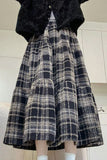 Person wearing a black and white plaid skirt with a dark jacket indoors.