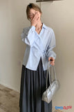 Person wearing a light blue shirt and dark gray skirt, holding a silver handbag indoors.