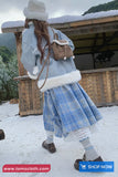 Person in winter clothing standing in a snowy landscape with a wooden structure.