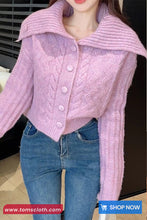 Person wearing a pink knitted cardigan and blue jeans with a blurred background
