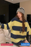 Woman wearing a yellow and blue striped sweater and gray beanie in an indoor setting.