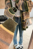 Person wearing a plaid sweater with green, brown, and yellow colors, standing indoors.