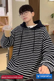 Person wearing a black and white striped hoodie holding a drink in an indoor setting.