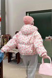 Person wearing a floral puffer jacket and pink hat, holding a pink handbag indoors.