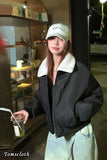 Person wearing a black jacket with white fur lining and a white cap, holding a drink, standing in front of a store.