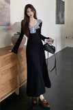 Woman in a black dress with lace details standing indoors.
