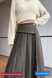 Person wearing a beige sweater and plaid skirt with a visible brand logo.