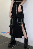 Person wearing a black outfit with a skirt and boots, holding a small bag, on a white background.