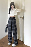 Person wearing a white sweater, plaid pants, and a cap in a room.