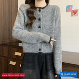 Person wearing a gray knitted cardigan with black buttons indoors.