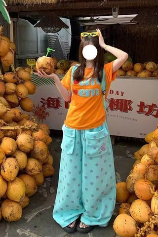 Person in an orange shirt and light blue pants standing among coconuts with a blurred face.
