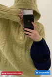 Person wearing a green cable knit sweater holding a phone with a white background