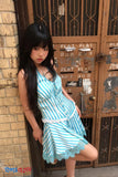 Woman in a blue striped dress standing against a brick wall with a metal gate.