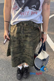 Person wearing a gray t-shirt with text, green camouflage skirt, and black shoes on a street.