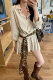 Woman wearing a beige shirt, white skirt, and brown boots with a leopard print belt in a room.