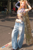Woman in a patterned top and blue jeans standing on a street with bicycles in the background.
