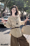 Woman in beige top and brown pants holding a beige handbag on a street.
