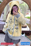 Person wearing a yellow hoodie with cat illustrations, taking a mirror selfie.