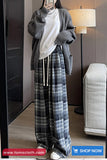 Person wearing a gray cardigan, white shirt, and plaid pants in a room with a lamp and sofa.