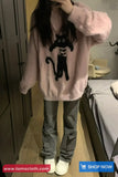 Person wearing a pink fluffy sweater with a black cat design, standing in a room.
