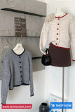 Two cardigans on mannequins with a handbag against a gray wall.