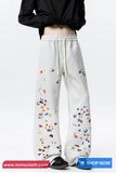 White sweatpants with colorful patterns worn by a person on a white background, with 'tomscloth.com' branding.